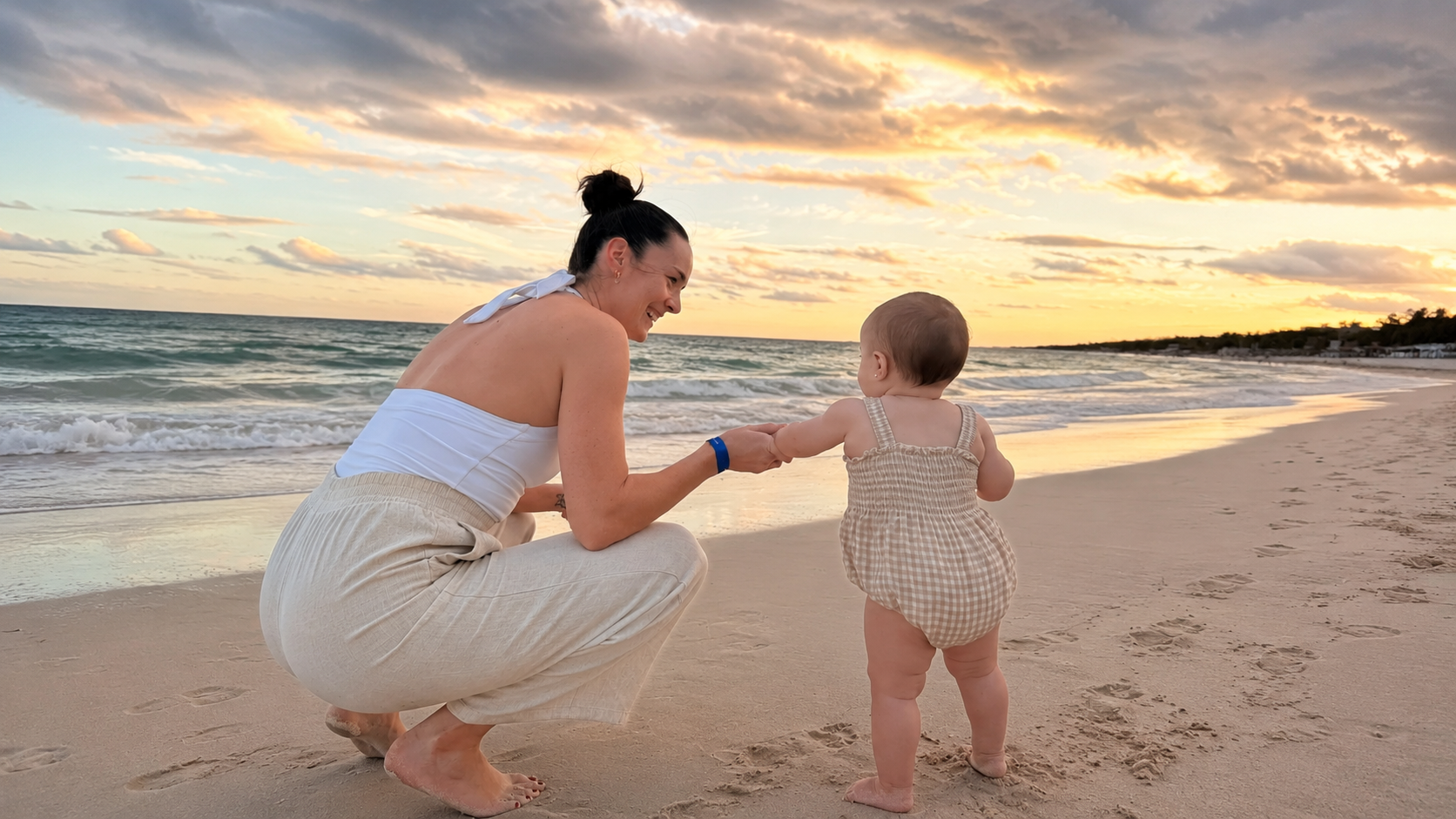 Maman accroupie tenant la main de son bébé sur la plage au coucher du soleil