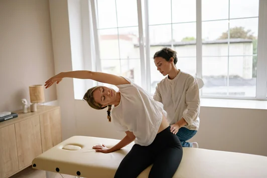 Physiothérapeute accompagnant une femme enceinte en étirement sur une table de traitement